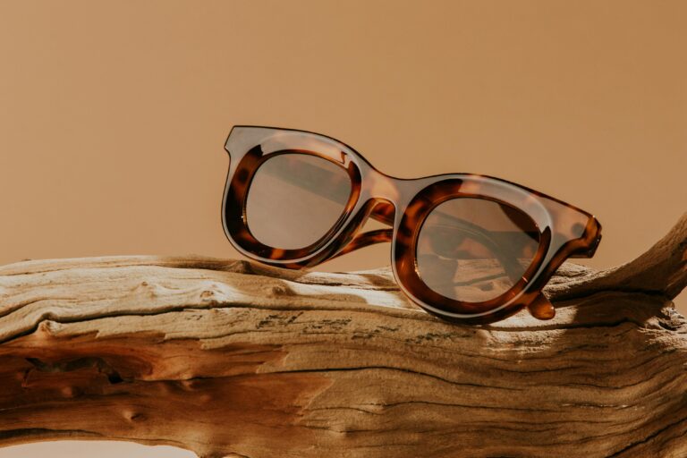 Stylish tortoiseshell sunglasses elegantly placed on natural driftwood against a beige backdrop.