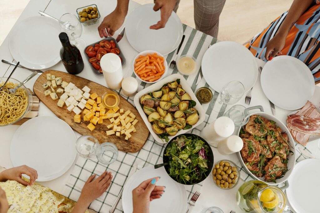 A top-down view of a diverse group's shared meal, featuring pasta, cheese, salad, and vegetables.
