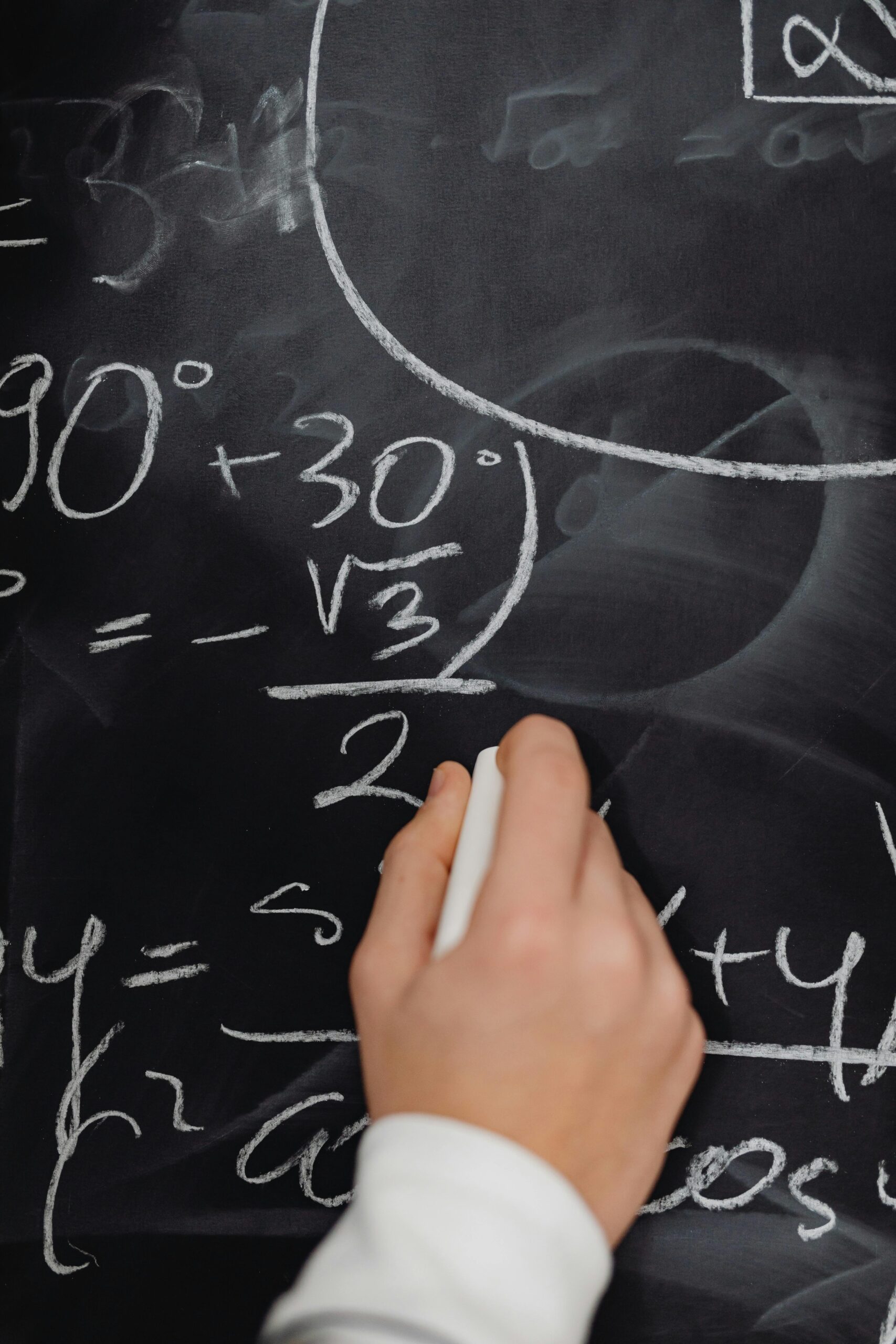Hand writing complex math equations on a blackboard in a classroom setting.