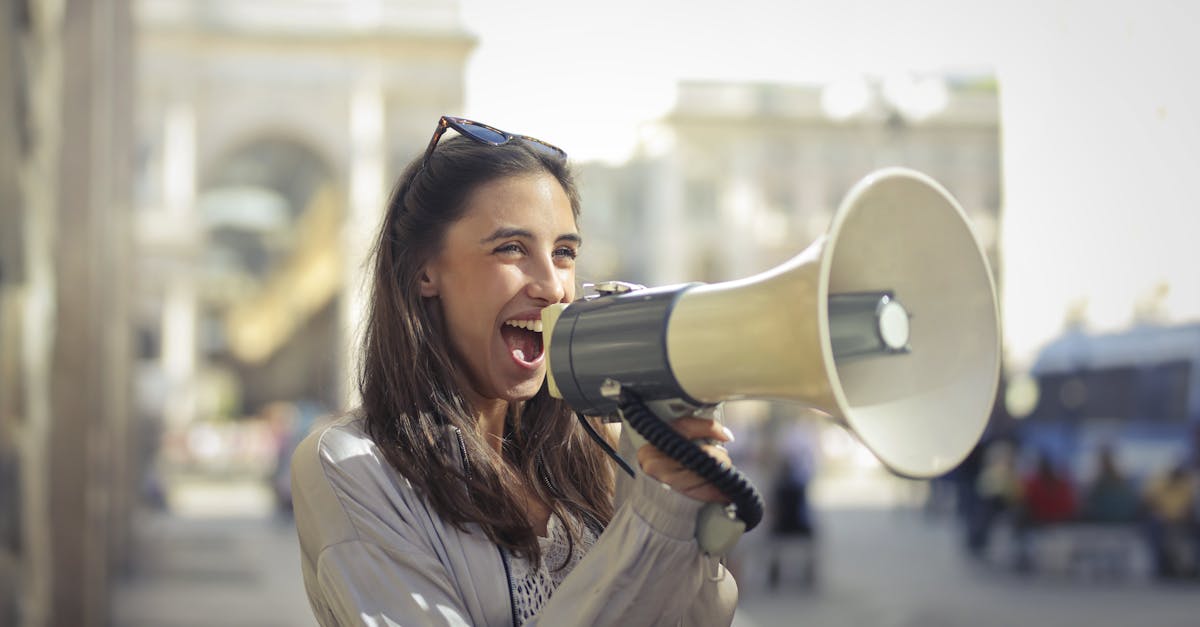 Cheerful young woman in a casual outfit shouting into a megaphone on a sunny day.