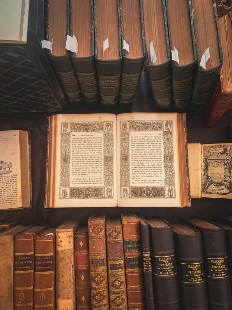 A collection of vintage books displayed in an antique library setting with an open ornate book highlighted.