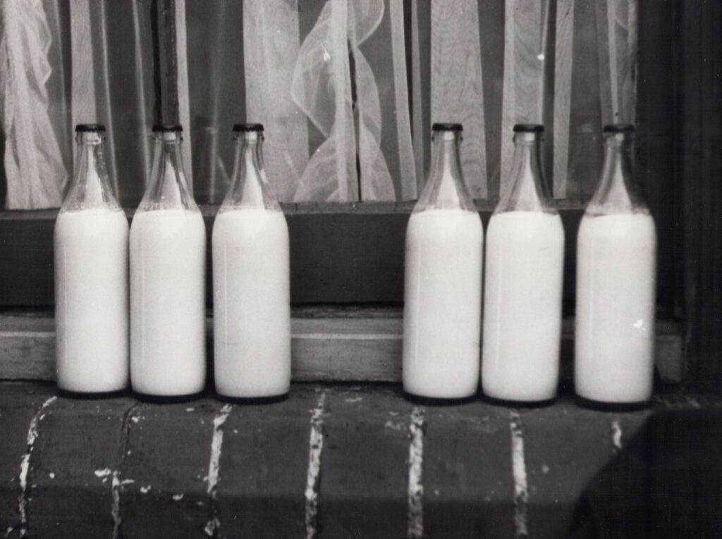 Vintage photo of glass milk bottles on a brick windowsill in monochrome.