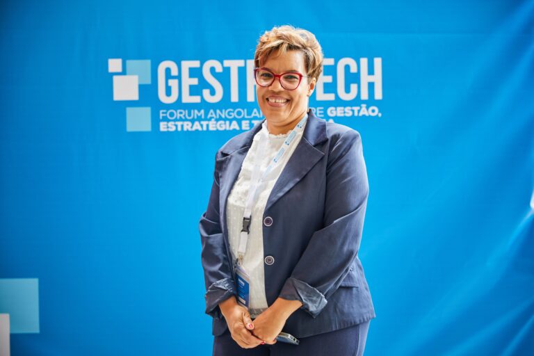 Businesswoman smiling in front of blue backdrop at trade fair event, embodying leadership and professionalism.